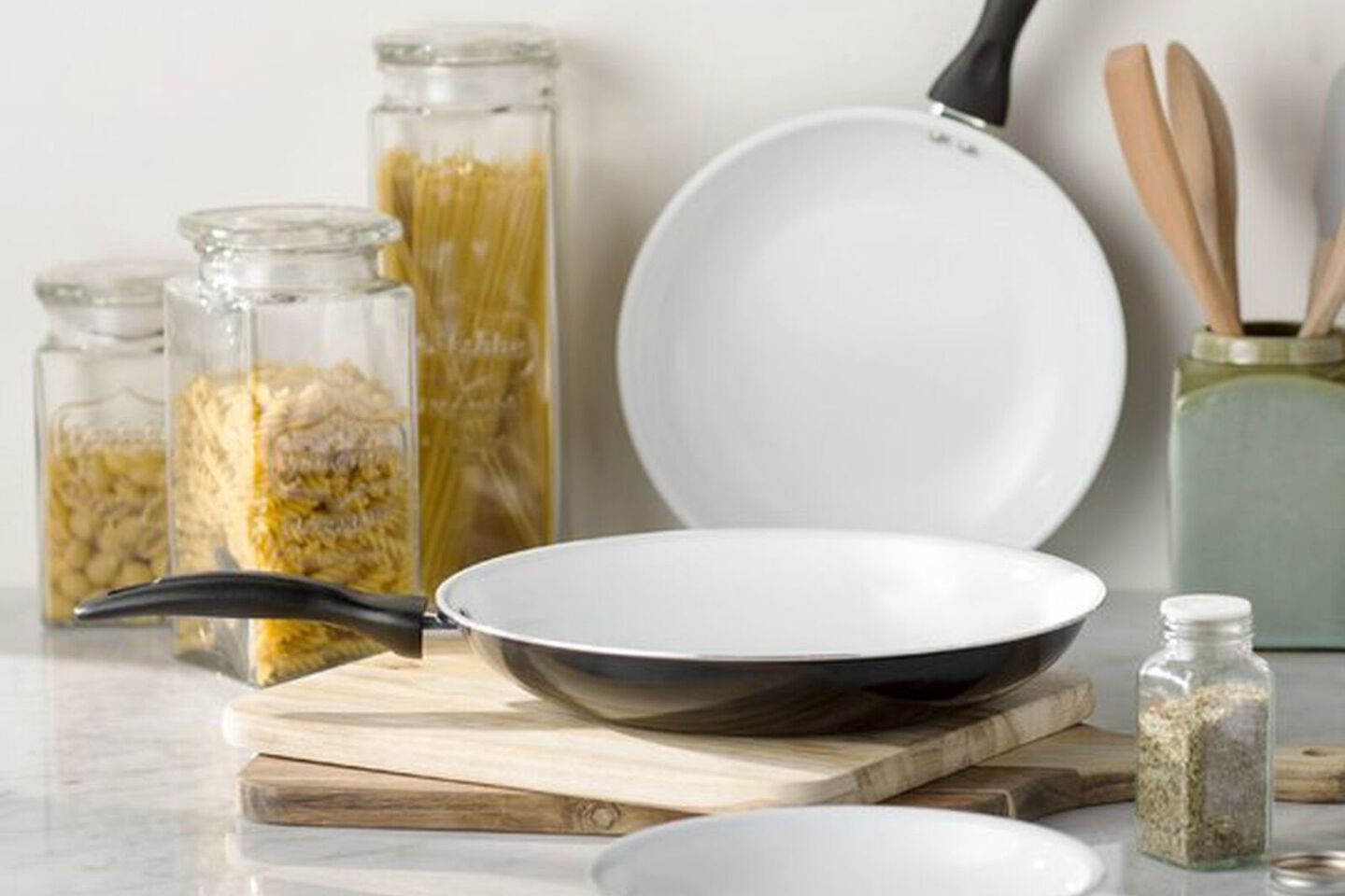Two black and white pans sitting on top of a cutting board next to glass storage containers