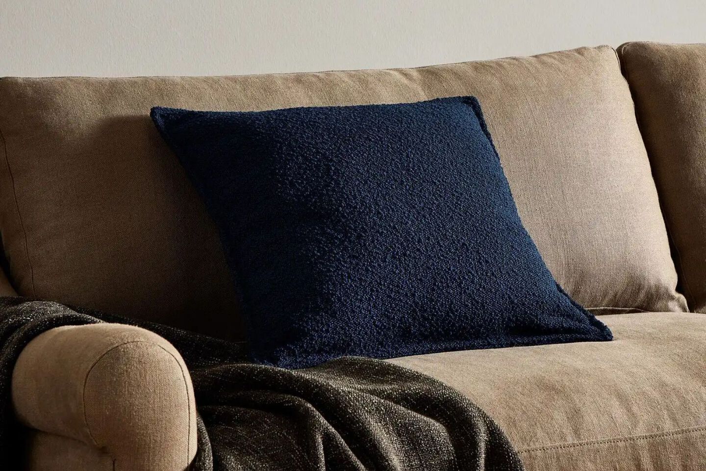 Single navy pillow sitting on a brown couch with a dark brown blanket