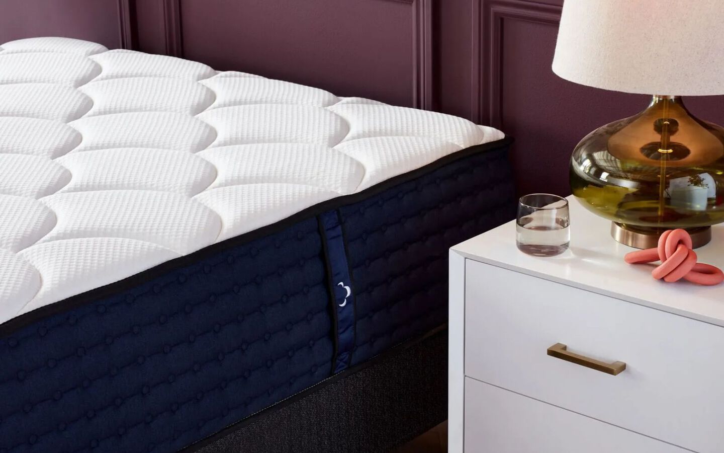 Close up of a navy and white mattress next to a white nightstand with a lamp