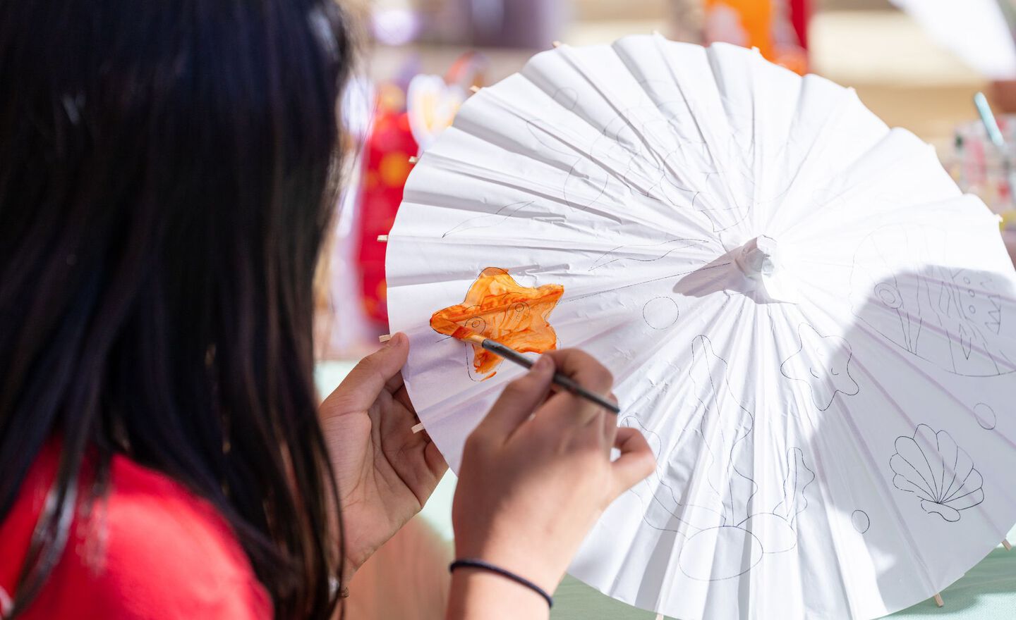 A young girl painting an orange star on a paper umbrella