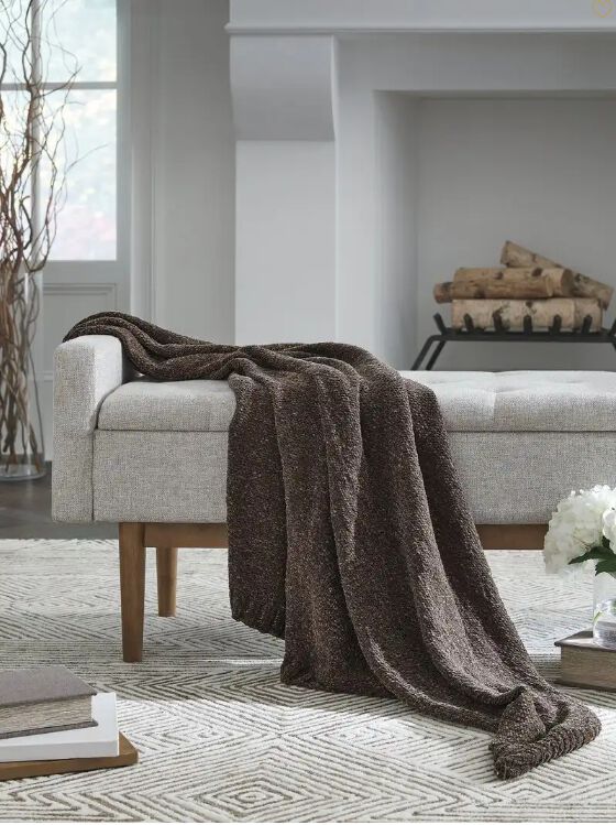 Brown blanket draped over a grey fabric bench in front of a fireplace.