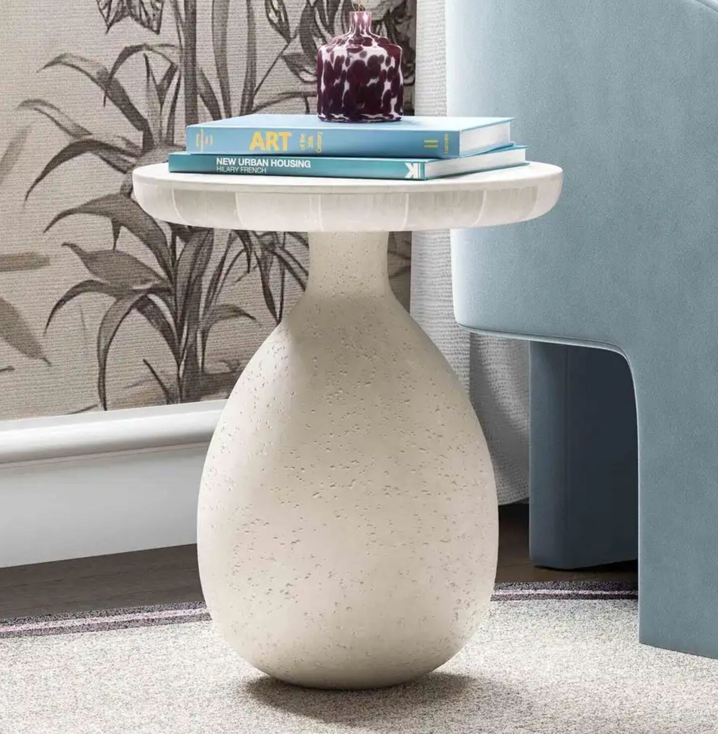 White stone table with two books sitting on top next to a blue velvet chair