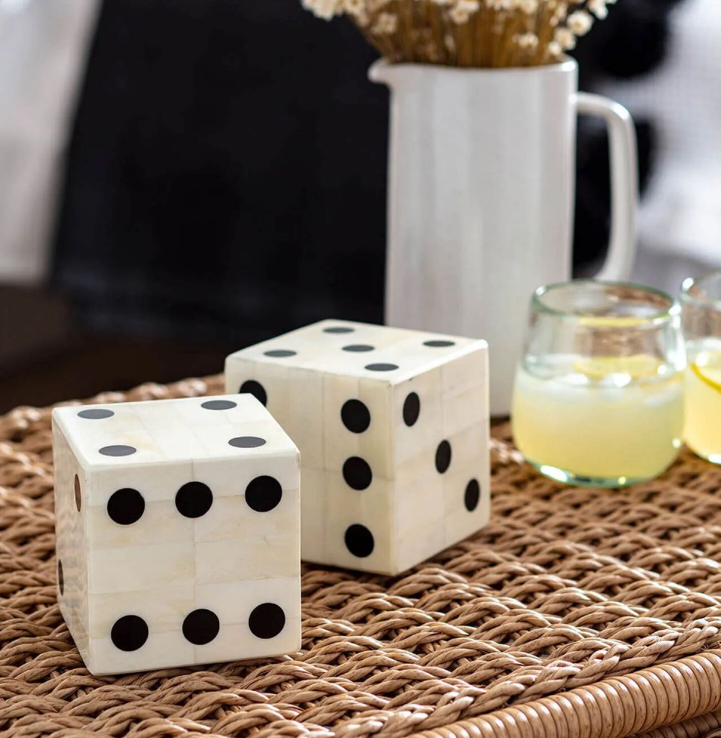 Two ivory and black oversized diced sitting on a woven brown table