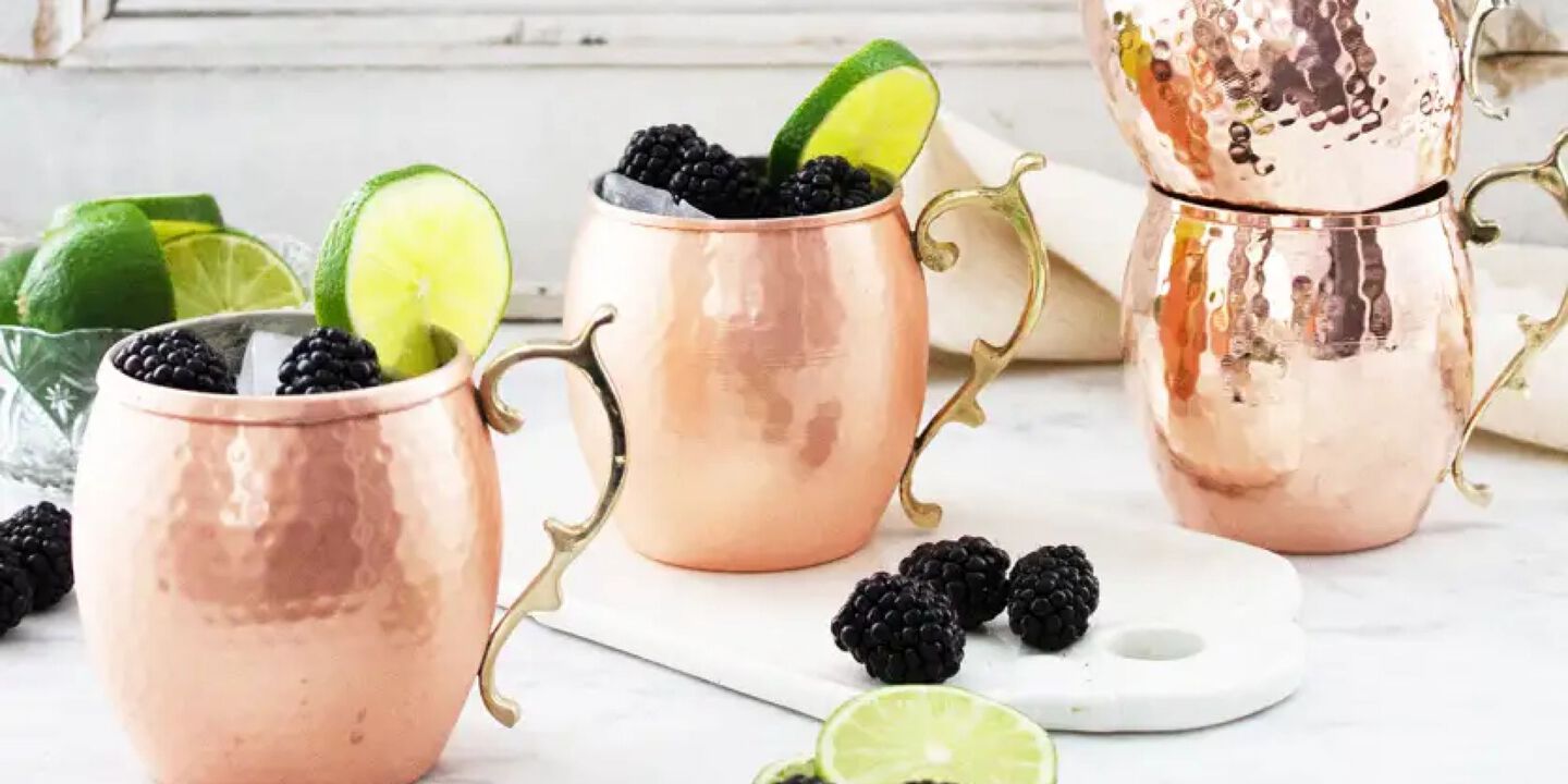 Kitchen counter with four brass moscow mule mugs on top filled with blackberries and limes