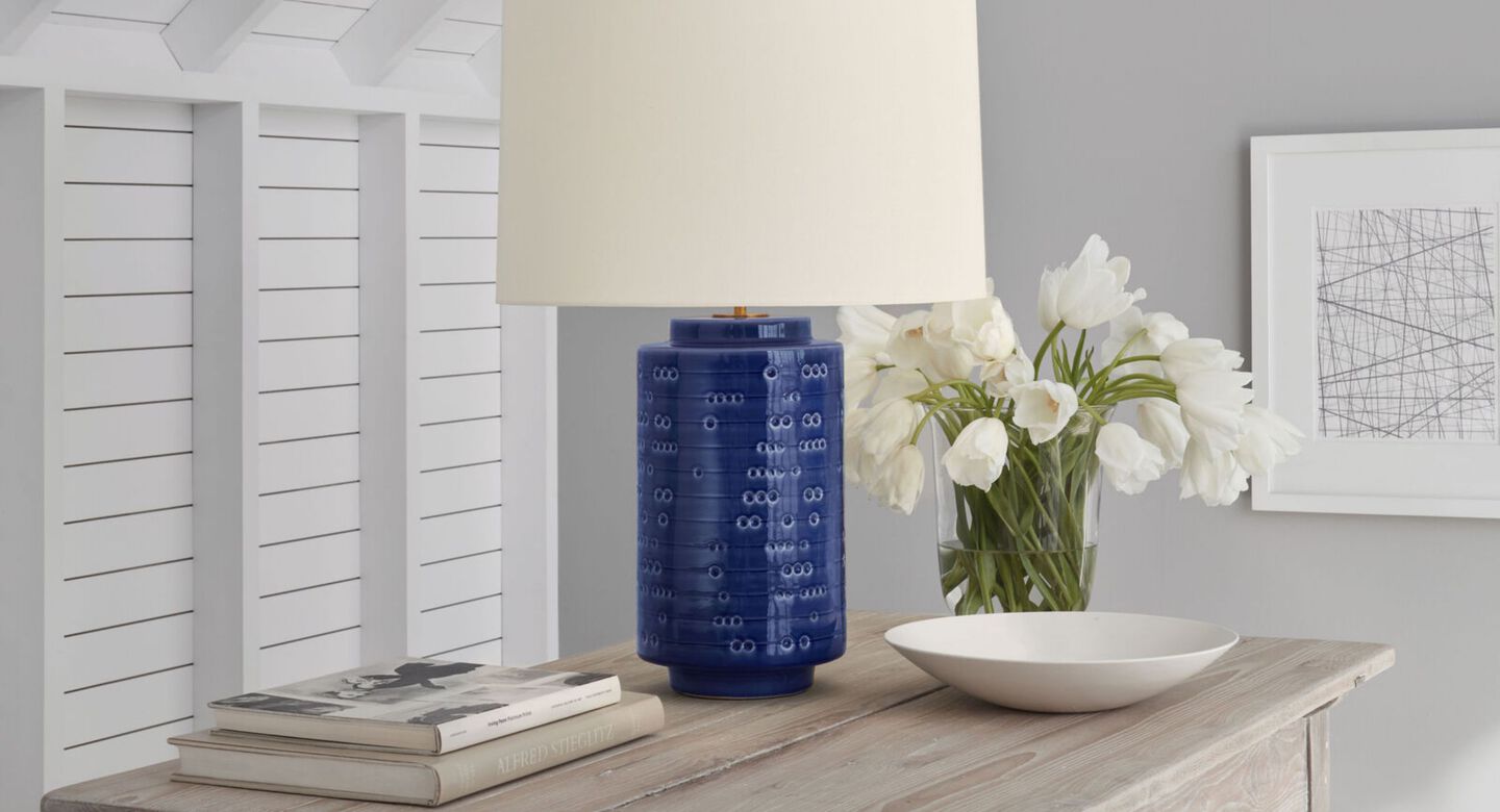 Side table with books, white flowers in a vase, and a blue and white lamp