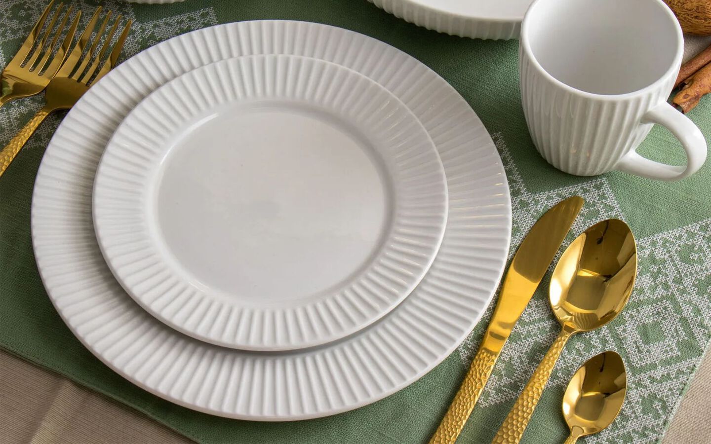 Place setting with white plates, matching cup, gold silverware, and green placemat