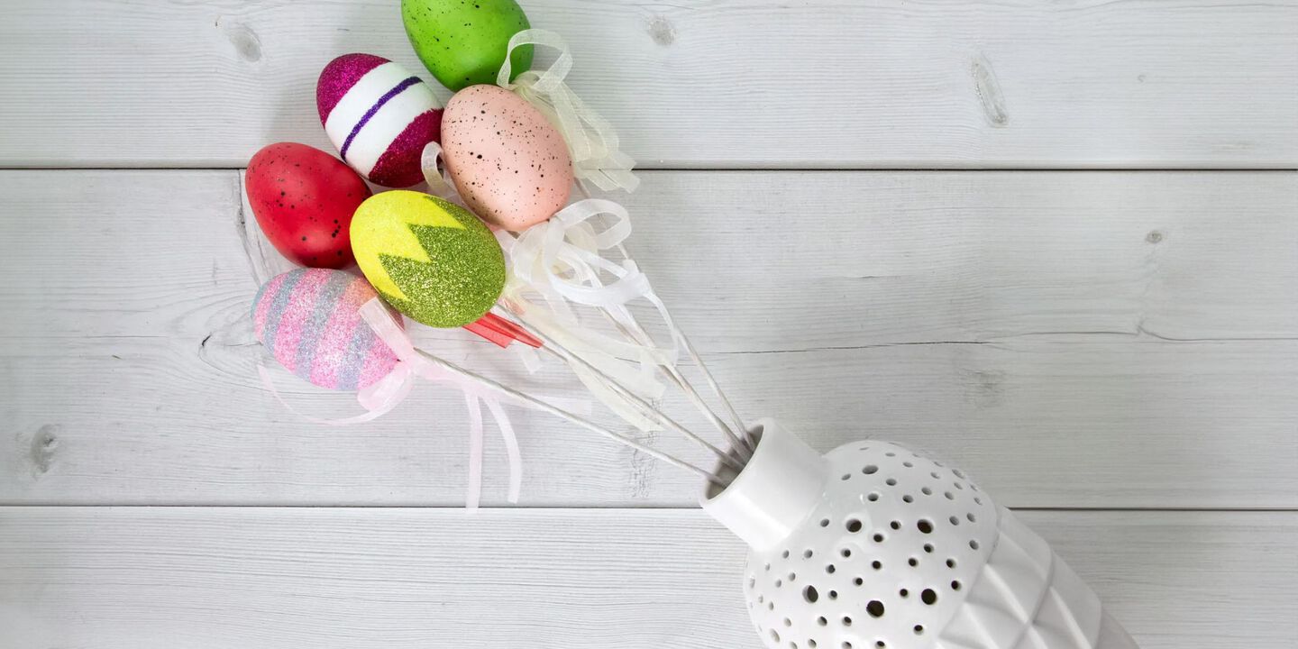Table with a white vase filled with colorful Easter eggs on sticks