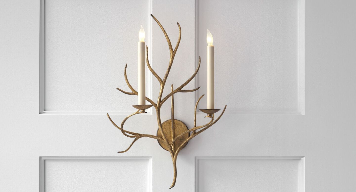 Gold branch-like lighting fixture with two candles hanging on a white wall