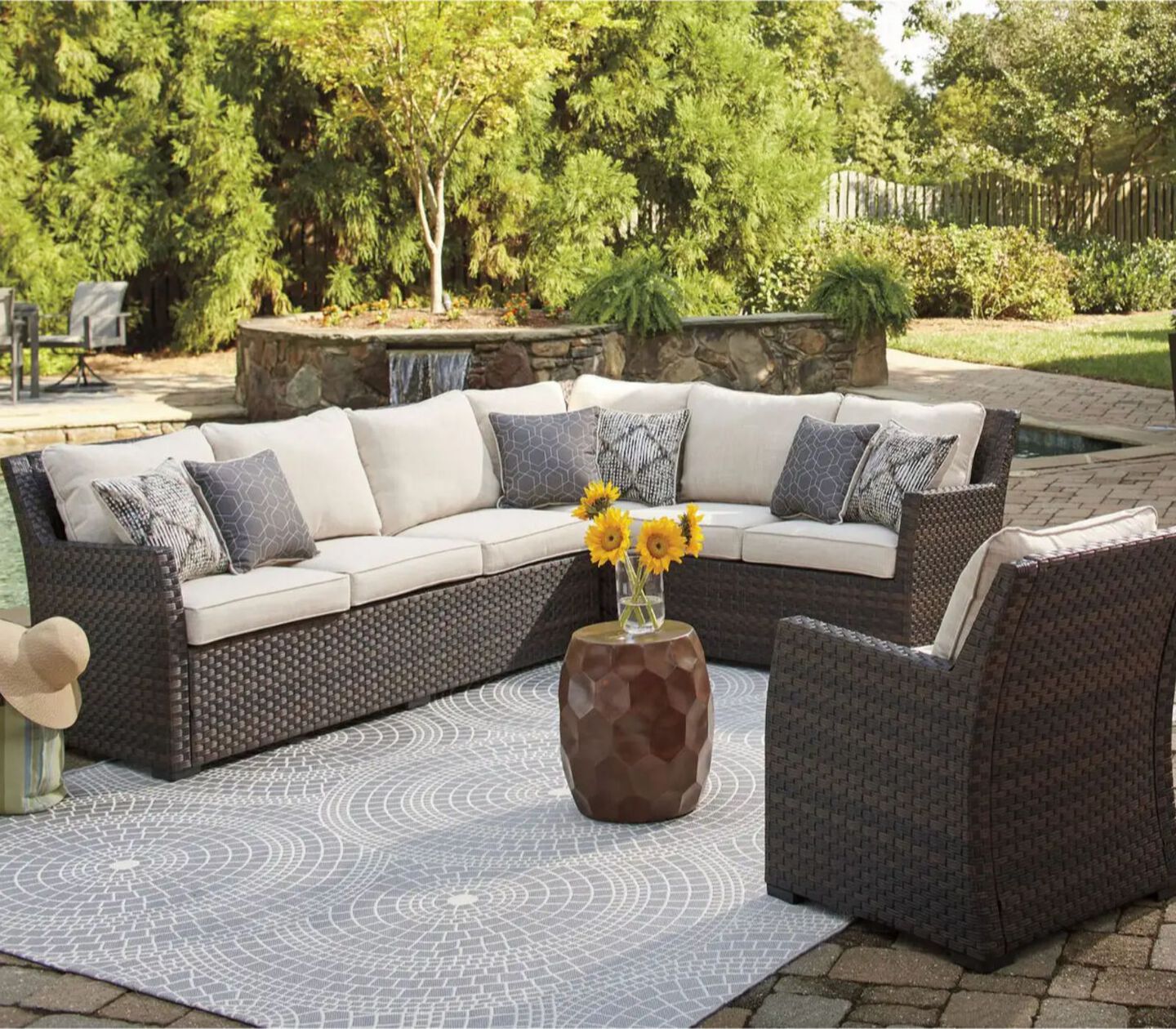 Brown patio sectional with light beige cushions surrounding small metal table with sunflowers