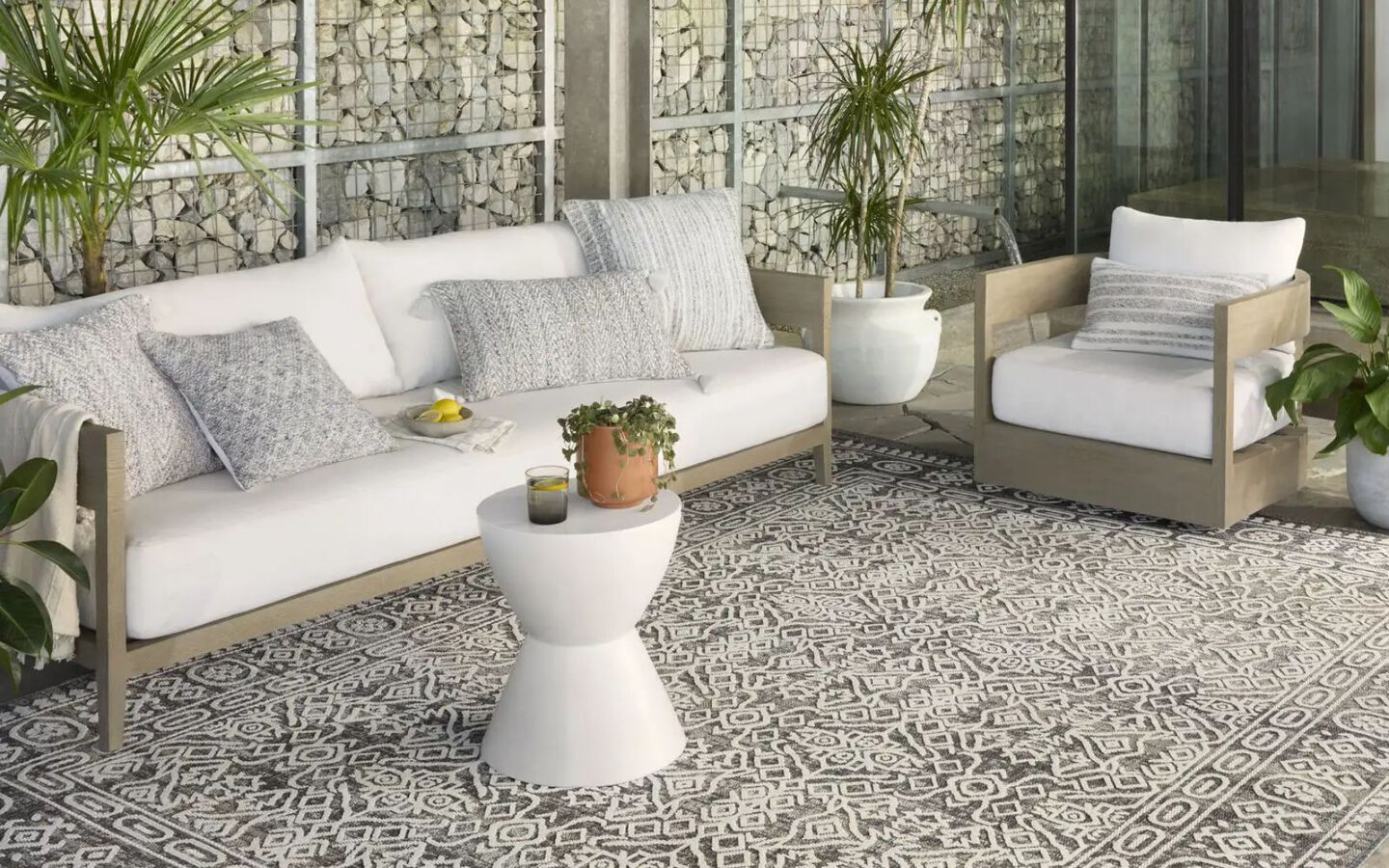 outdoor patio with white and light wooden furniture and a dark grey and white patterned rug