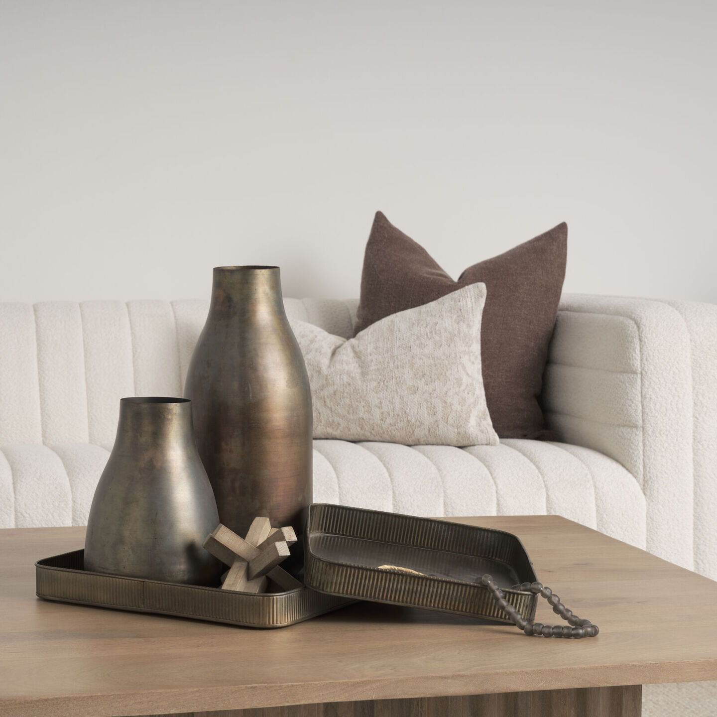 Two antique bronze vases and a small wooden decorative object arranged on a dark metal ribbed tray on a wood coffee table.