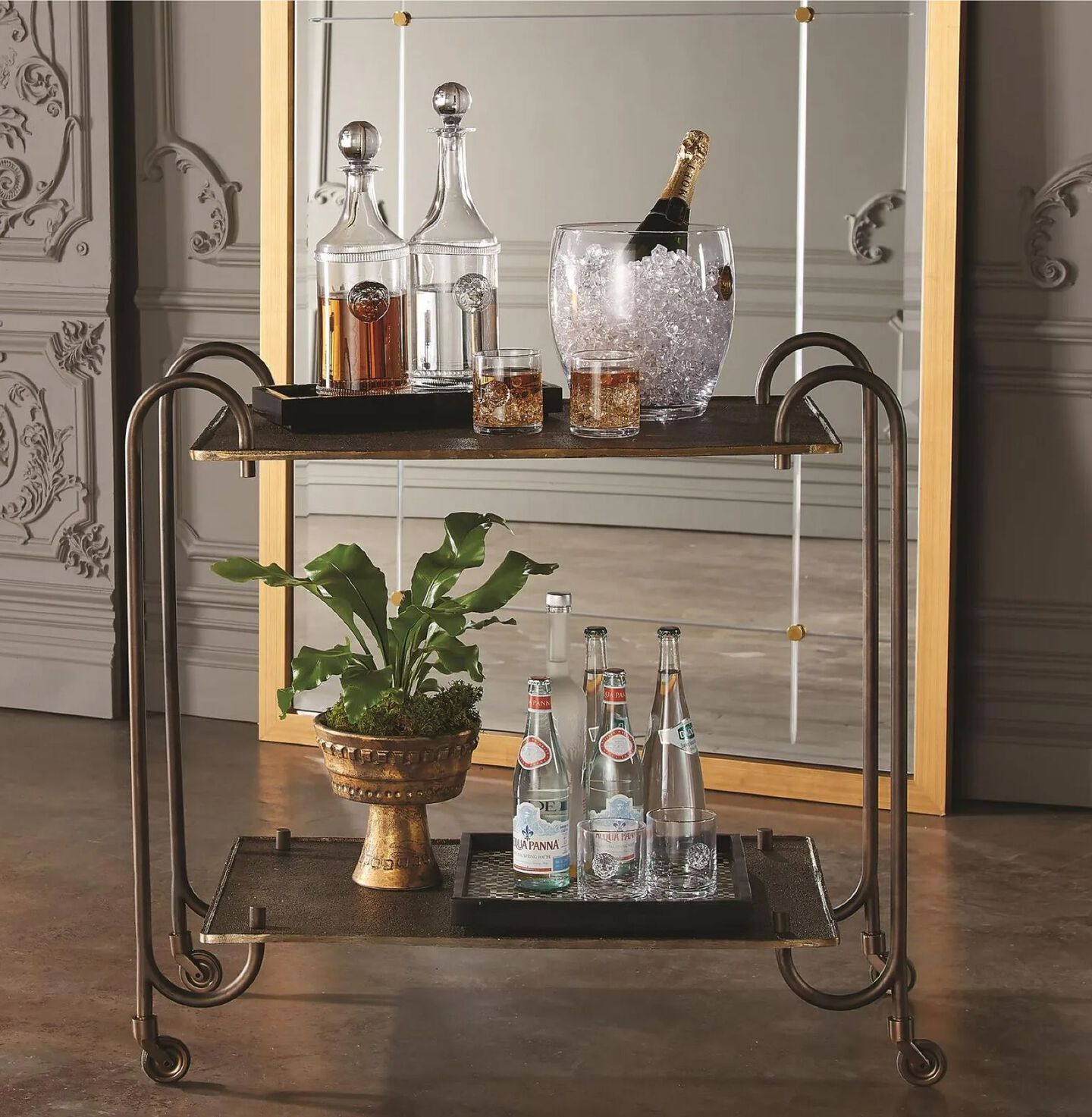 Bronze metal bar cart with arching legs sitting in a room in front of a mirror