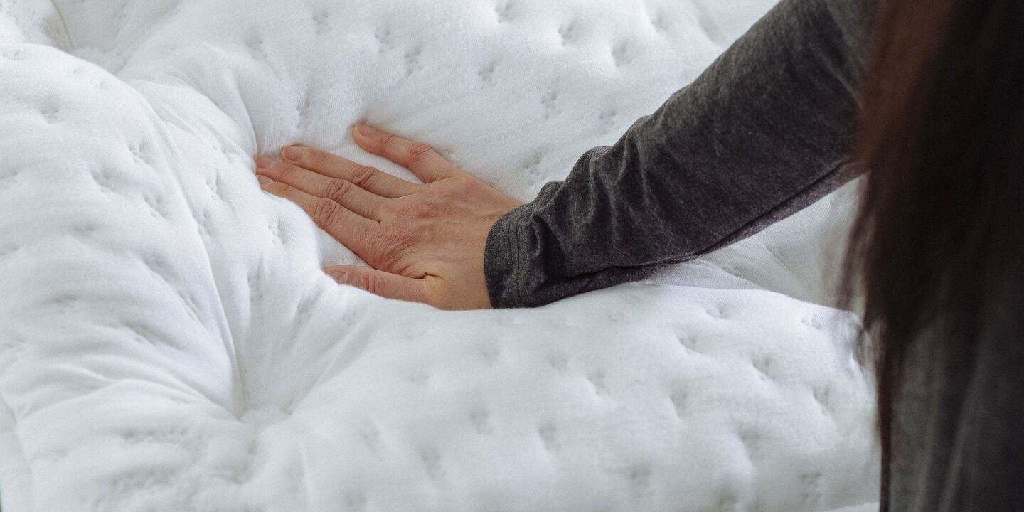 Hand pushing into a white padded mattress