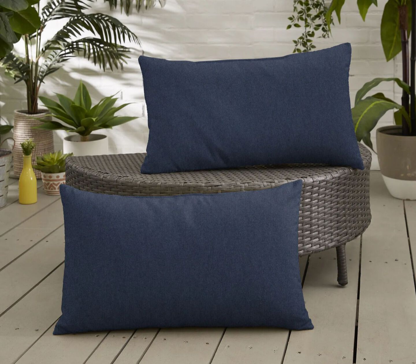 Two navy pillows placed upright on a patio and ottoman
