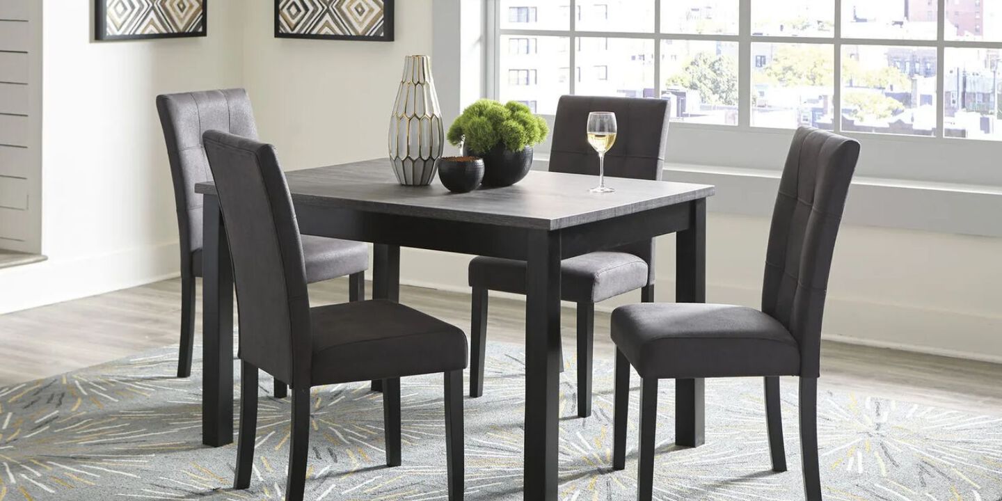 Dining room set with black table surrounded by four upholstered black chairs, and white vase and fake plant on top