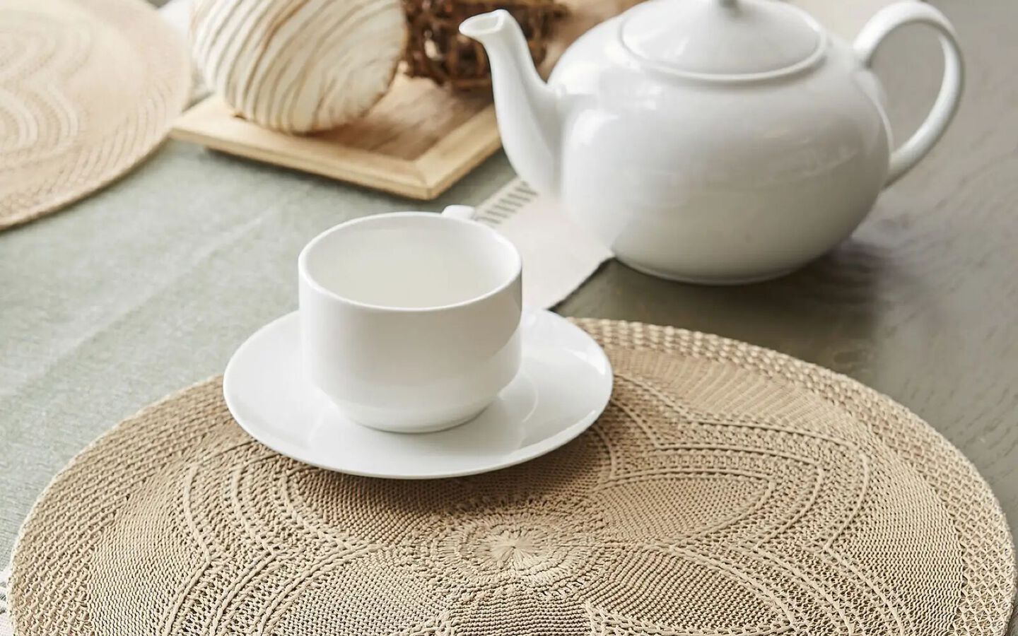 Placemat with white teacup and plate sitting on top next to a matching white teapot
