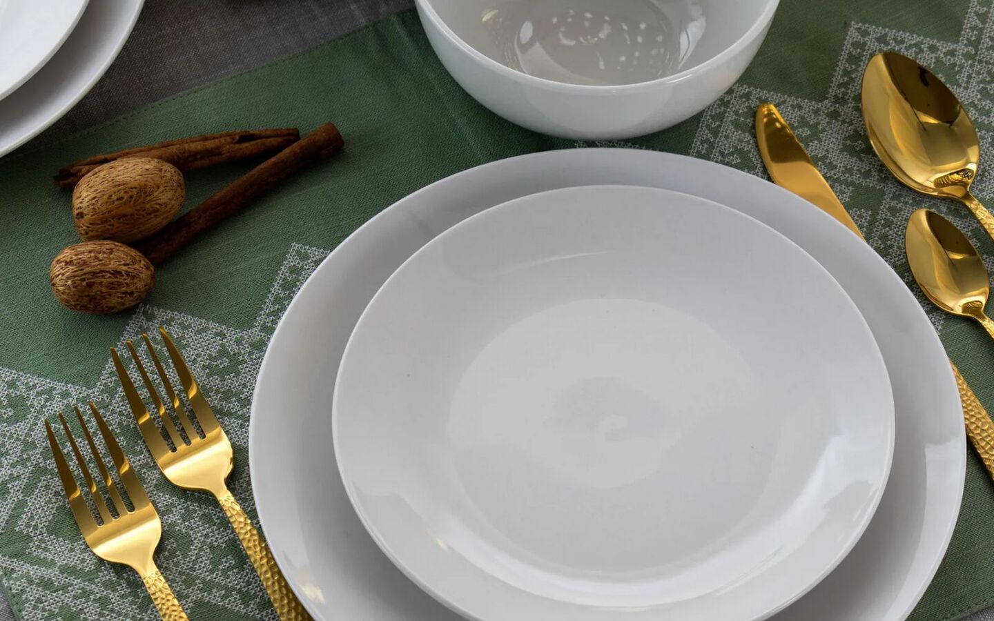 Place setting with white plates, matching bowl, and gold silverware on a green placemat