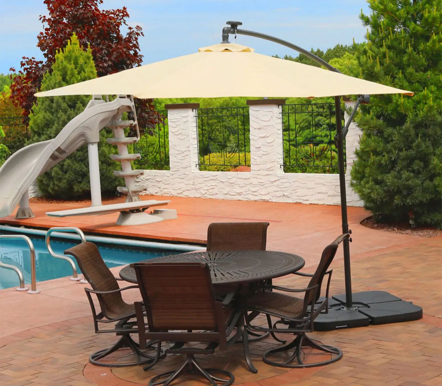 Brown and black patio table and chairs covered by a beige standing umbrella