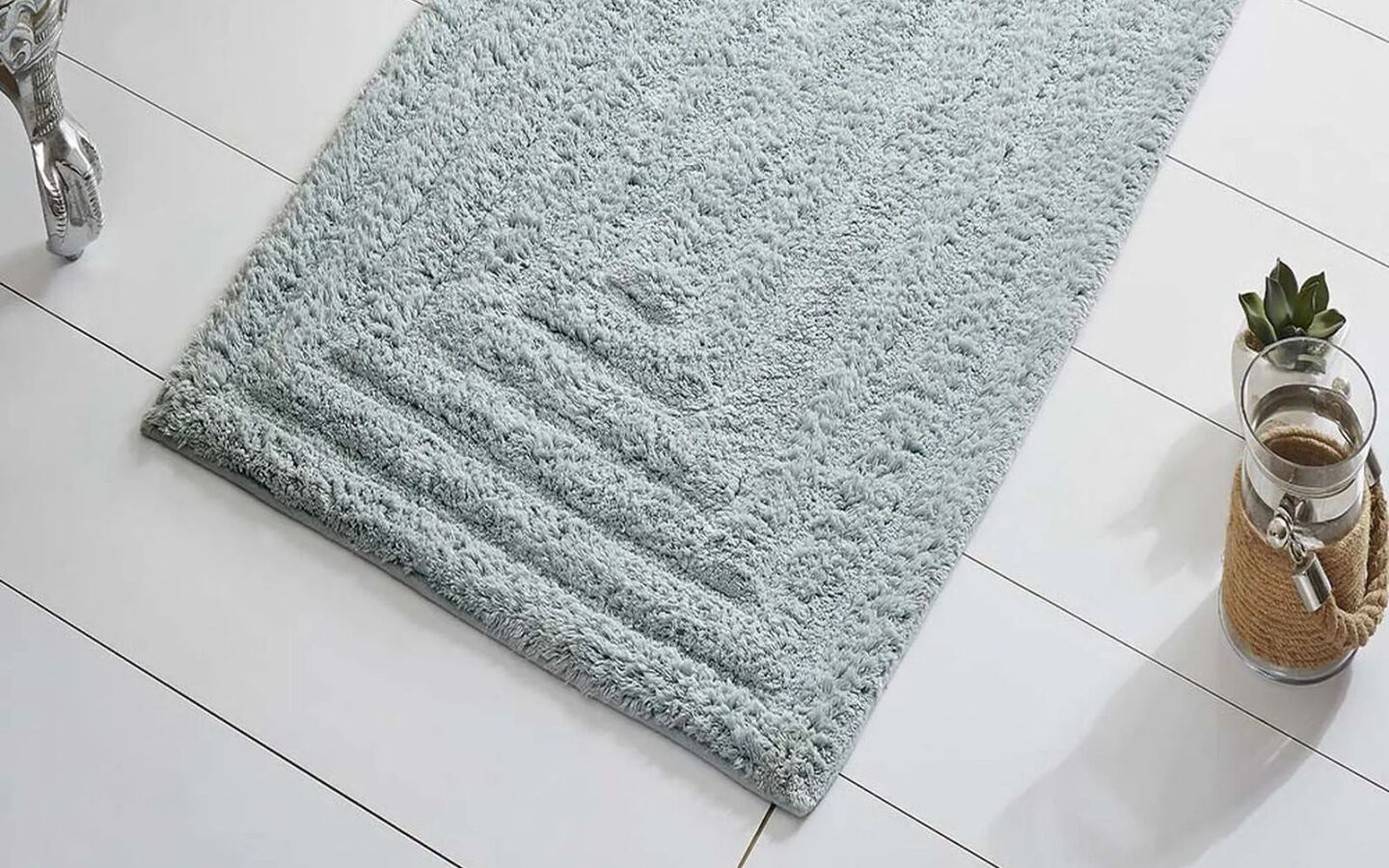 Light blue bathmat on white tiled bathroom floor