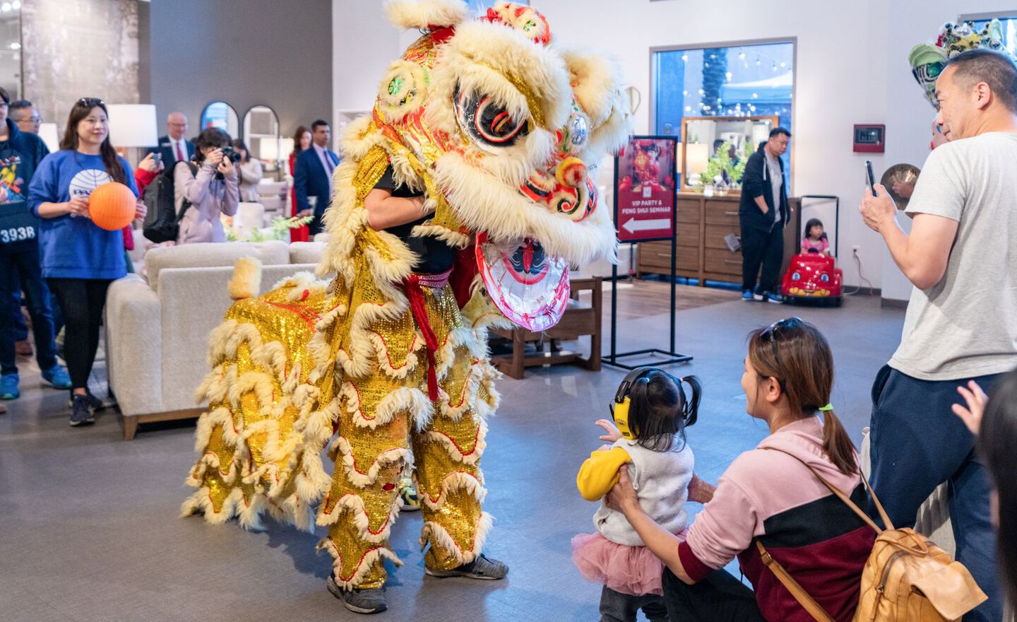 A man in a dancing dragon costume interacting with a small child and her mother