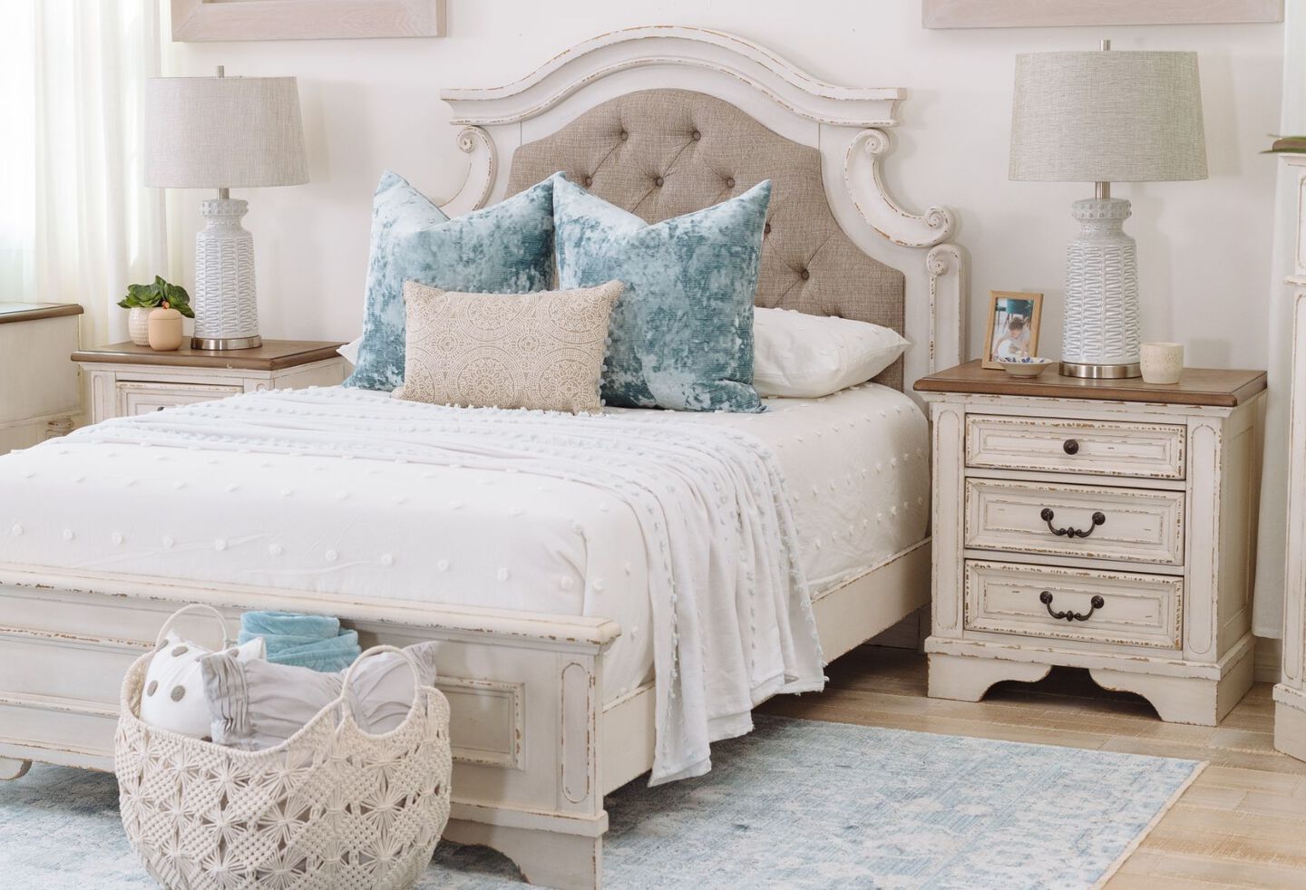 Bedroom with off-white bed with blue and tan pillows and a light wooden nightstand