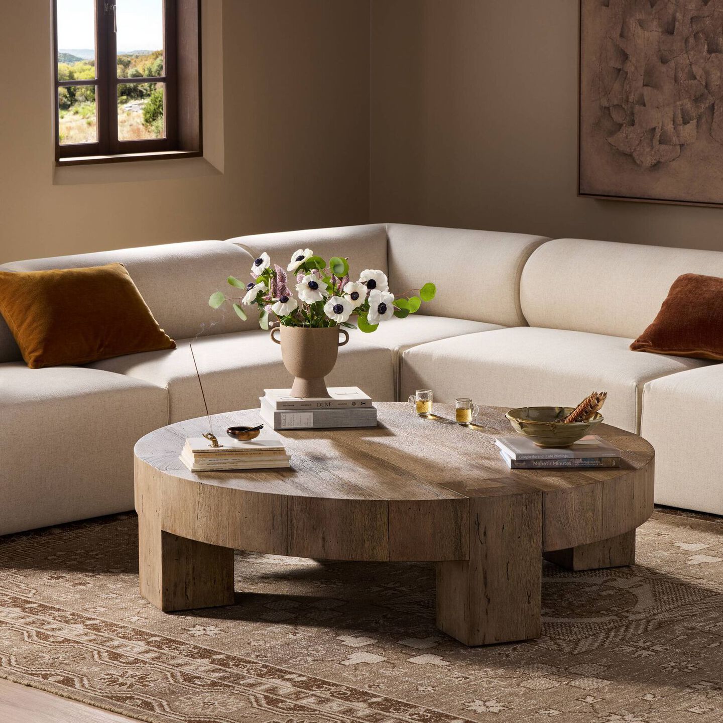 Traditional round coffee table with decoratively placed book stacks, a vase with flowers, and two tea cups.