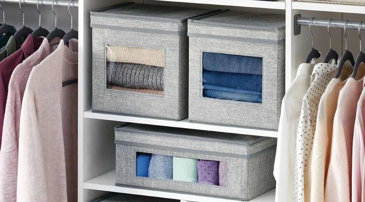 Grey organizational cubes filled with clothes sitting on a closet shelf