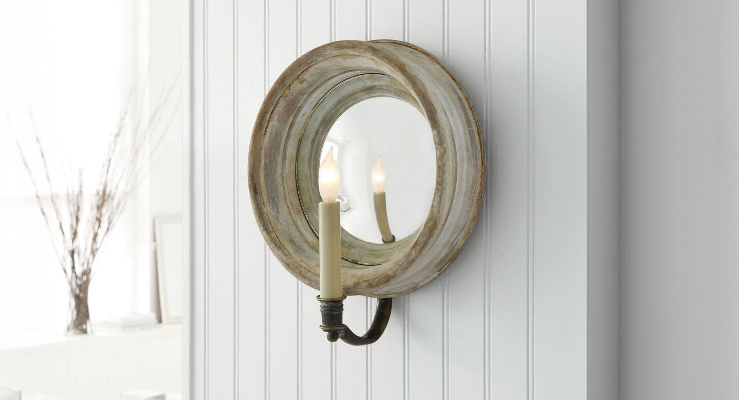 Grey distressed light fixture with mirror hanging on a white paneled wall