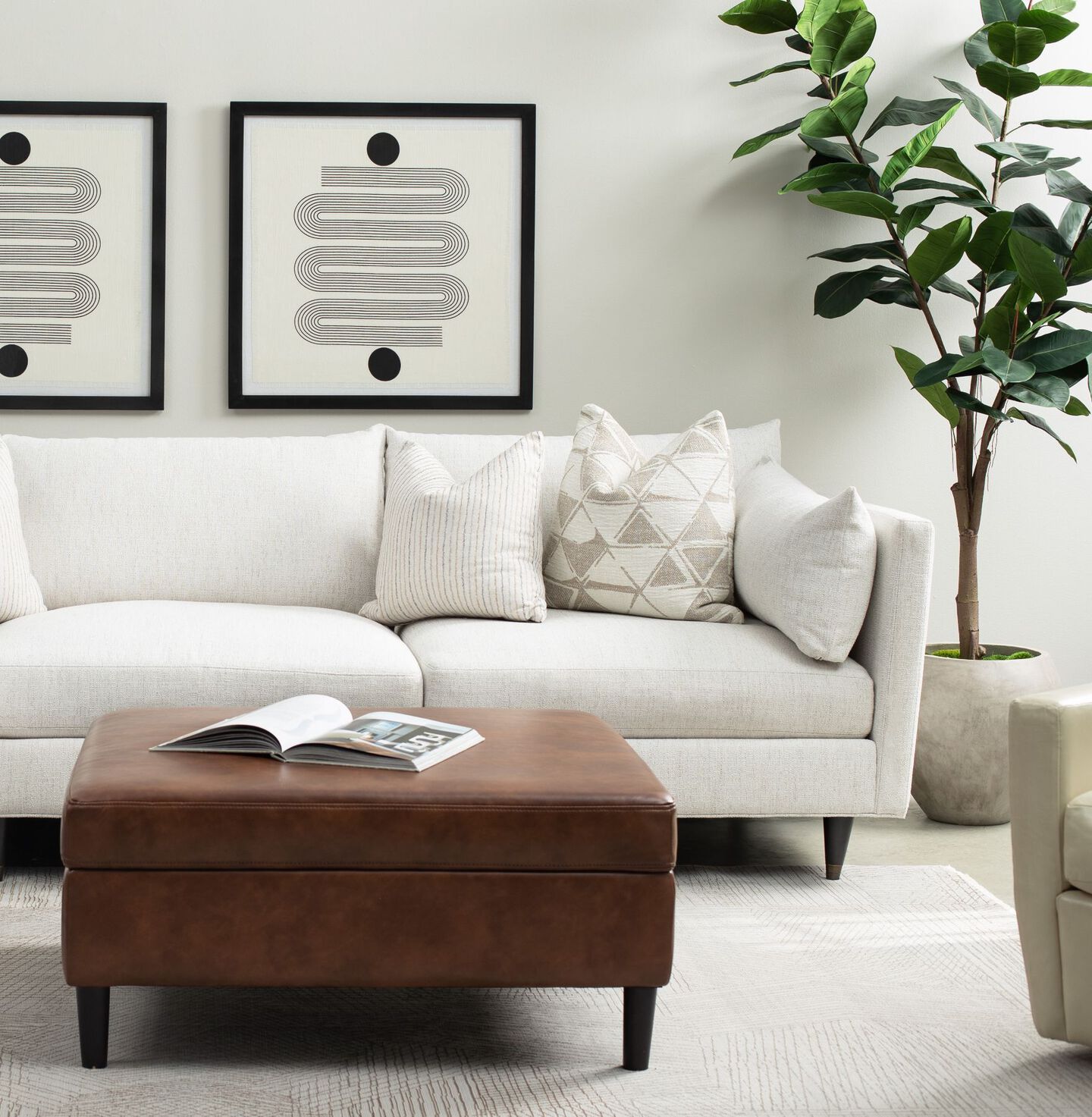 Living room with brown leather ottoman and a white couch with white and cream pillows