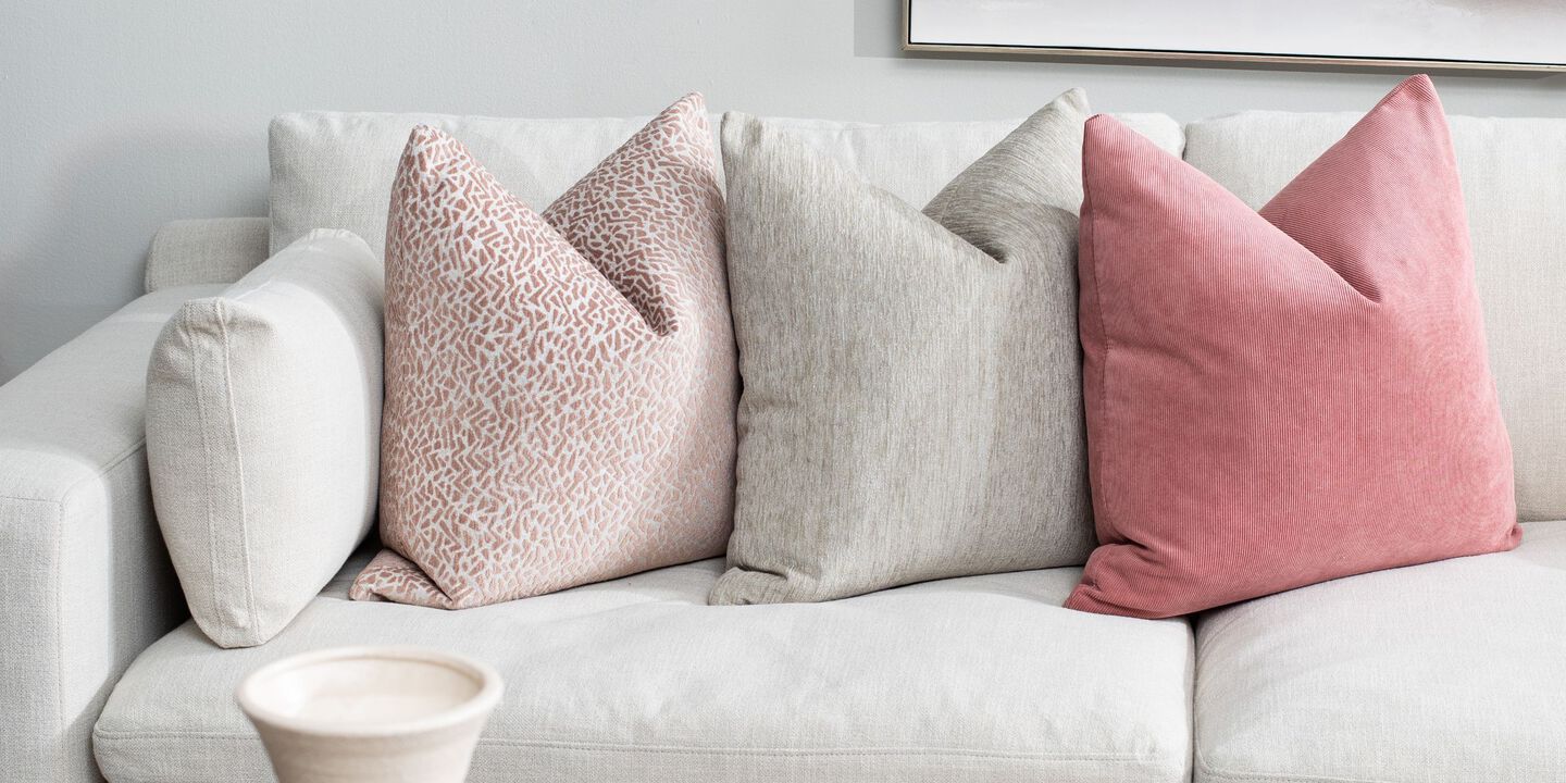 Light grey couch with three pillows on top, two pink and one light grey