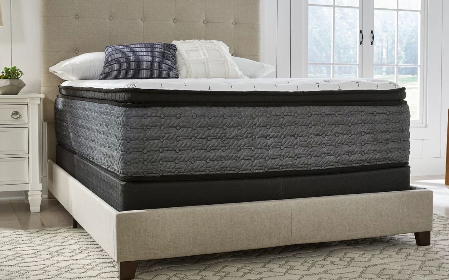 Close up image of the bottom edge of a grey mattress on a beige bedframe