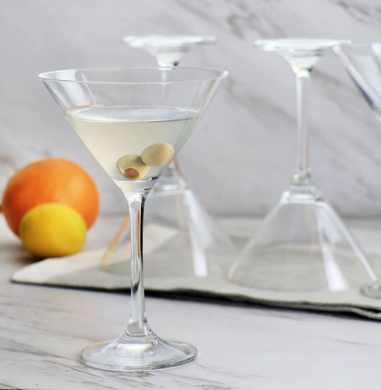 Glass martini glass with two olives sitting next to two upside down matching glasses