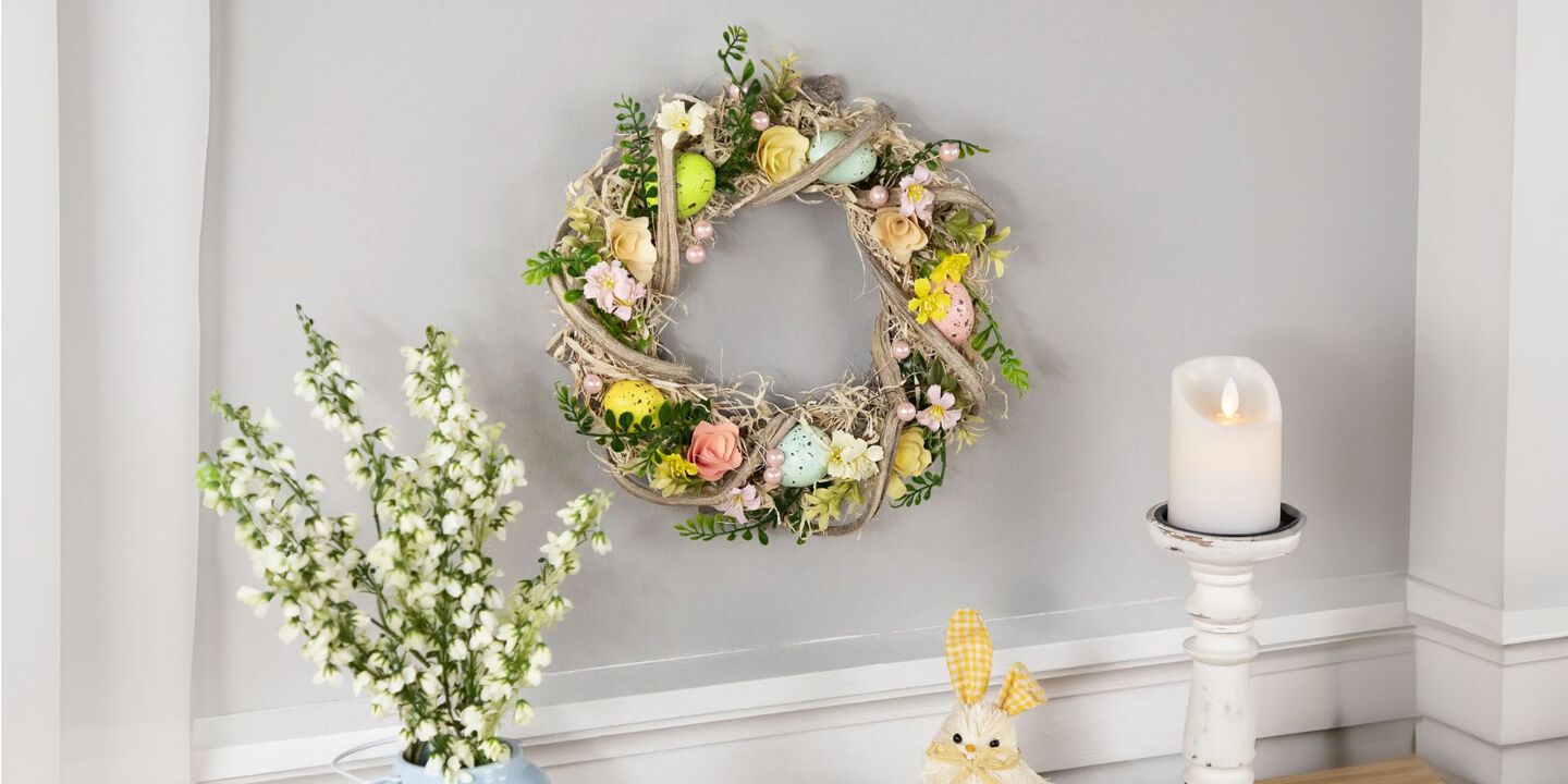 Light grey wall with a pastel-colored Easter egg wreath hanging on it