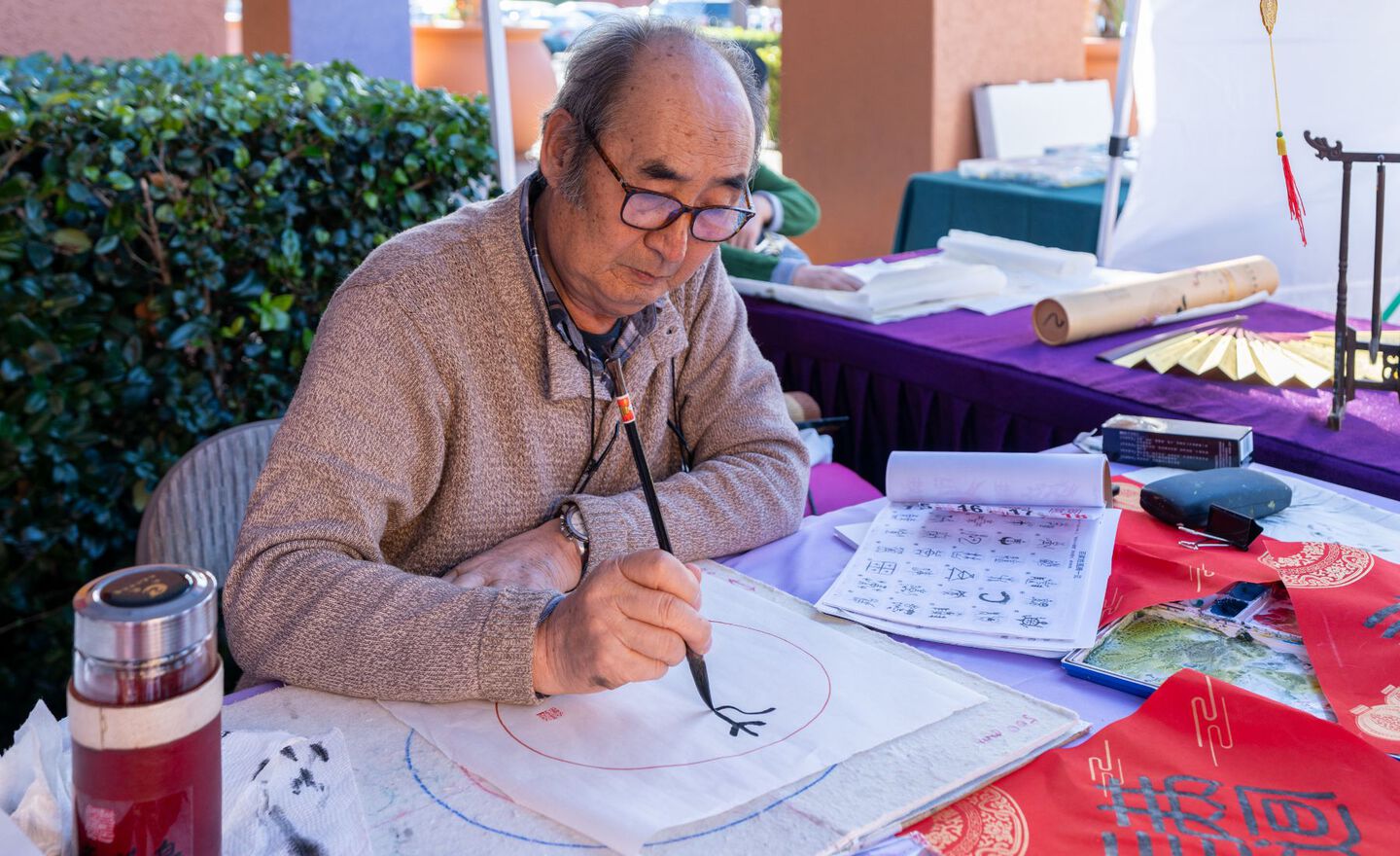 A man painting calligraphy couplets within a circle on a piece of paper
