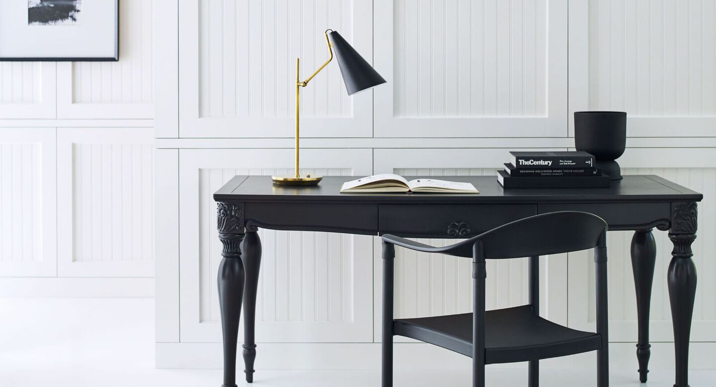 Black and gold lamp sitting on top of a solid black desk with a matching black chair