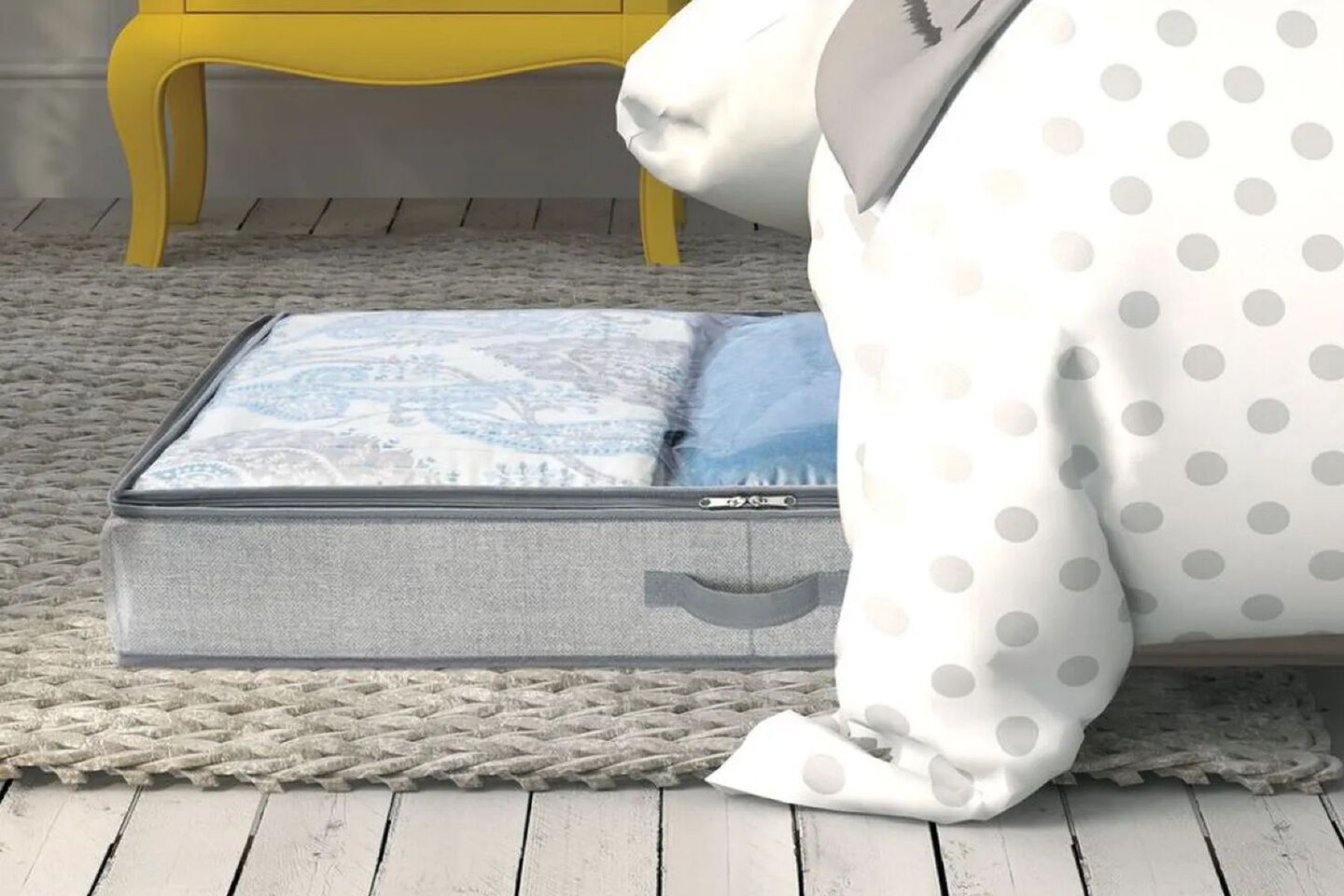 Grey and clear storage bin filled with sheets sticking out from under a bed