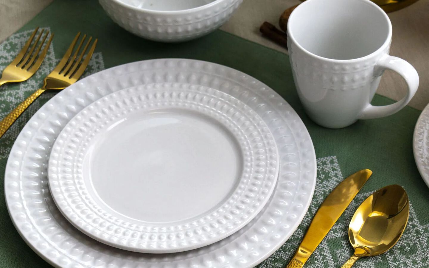 Closeup of white plate setting, matching cups, and gold silverware on a green placemat