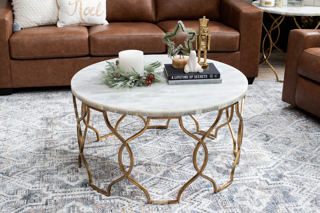 The Corrina Cocktail Table is distinguished by a delicate fretwork metal base in a gold leaf finish topped by a round white onyx top of organic elegance.